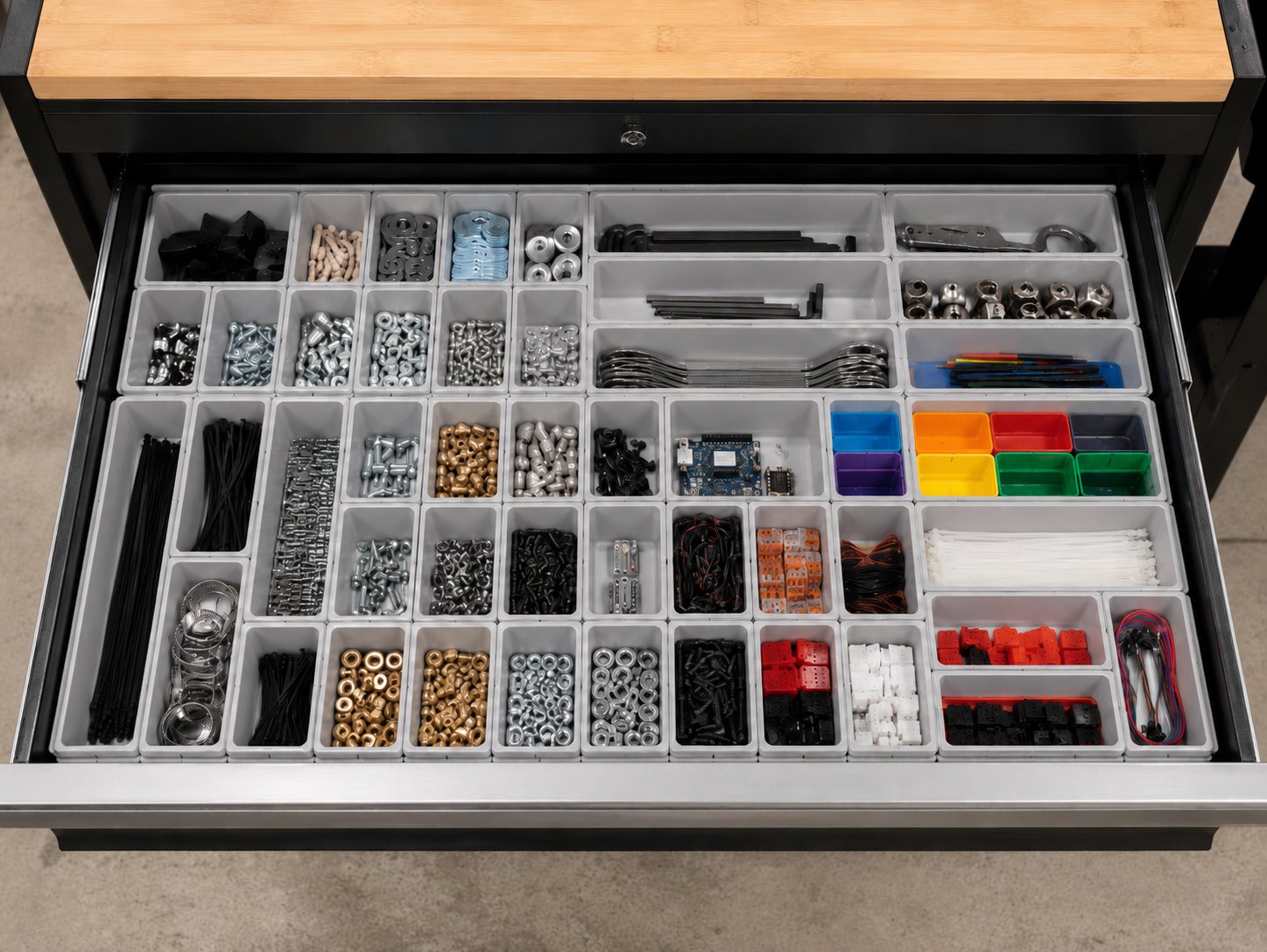 A drawer of gray Gridfinity bins holding hardware, with bright empty bins in blue, orange, red, purple, yellow, and green